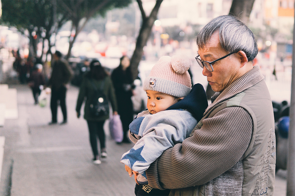 Older man carrying young infant in his arms.